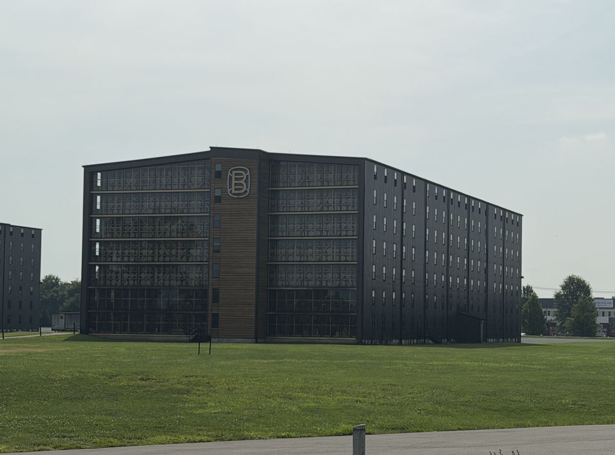 Bardstown Bourbon Company black rickhouse with the B logo above a green lawn