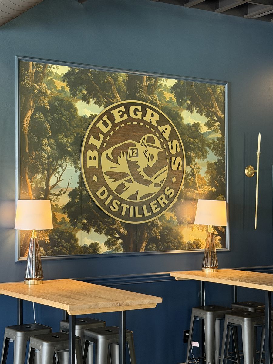 Bluegrass Distillers logo mural on a navy wall above high top tables and stools