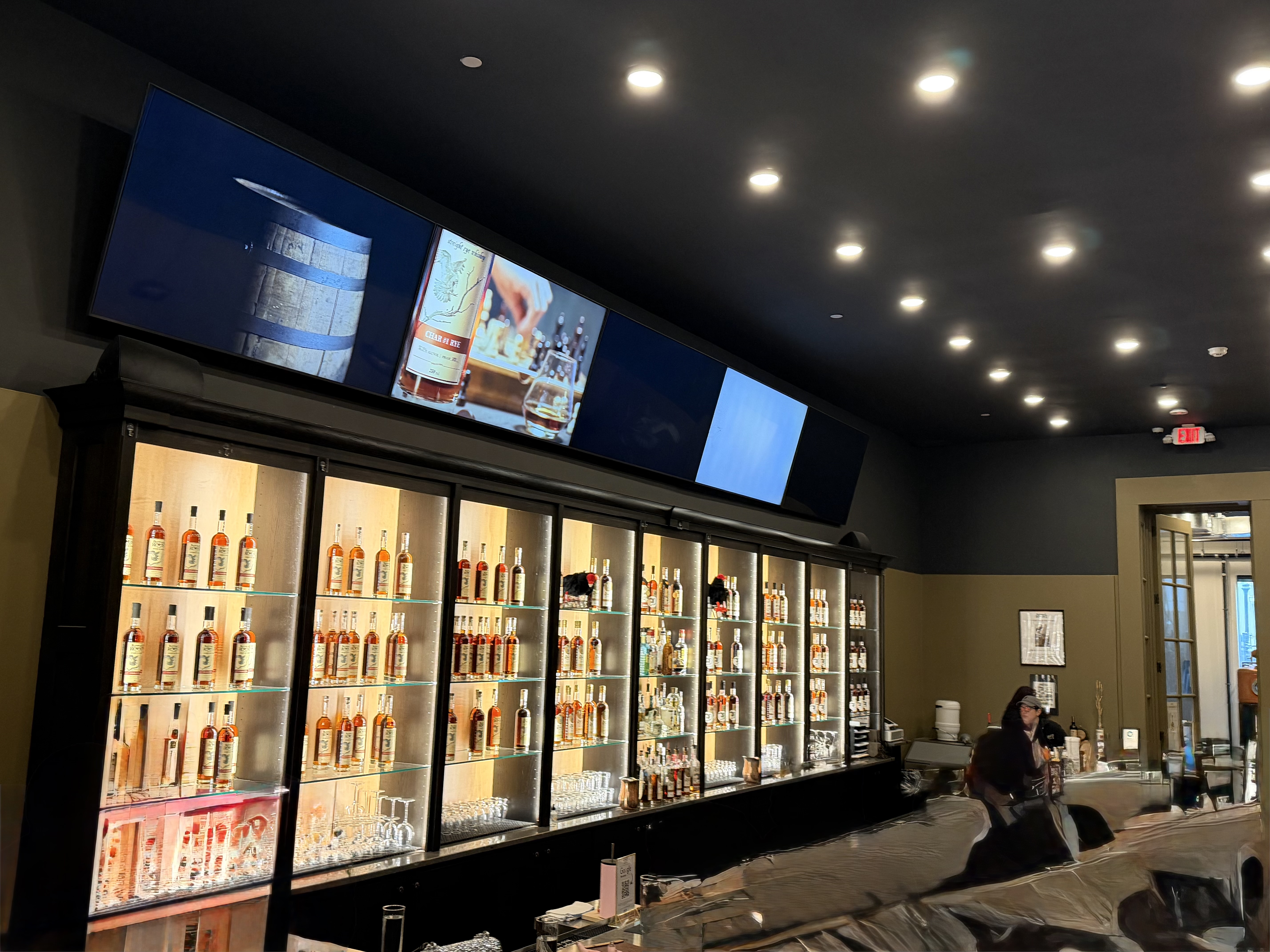 Illuminated back bar at Buzzard's Roost with full glass cases of whiskey bottles and barrel education screens above