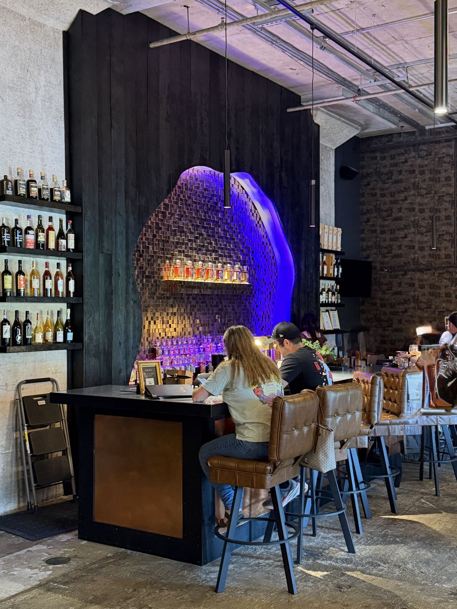 Dark Arts bar with guests seated at a counter under purple lighting and a wall of bottles