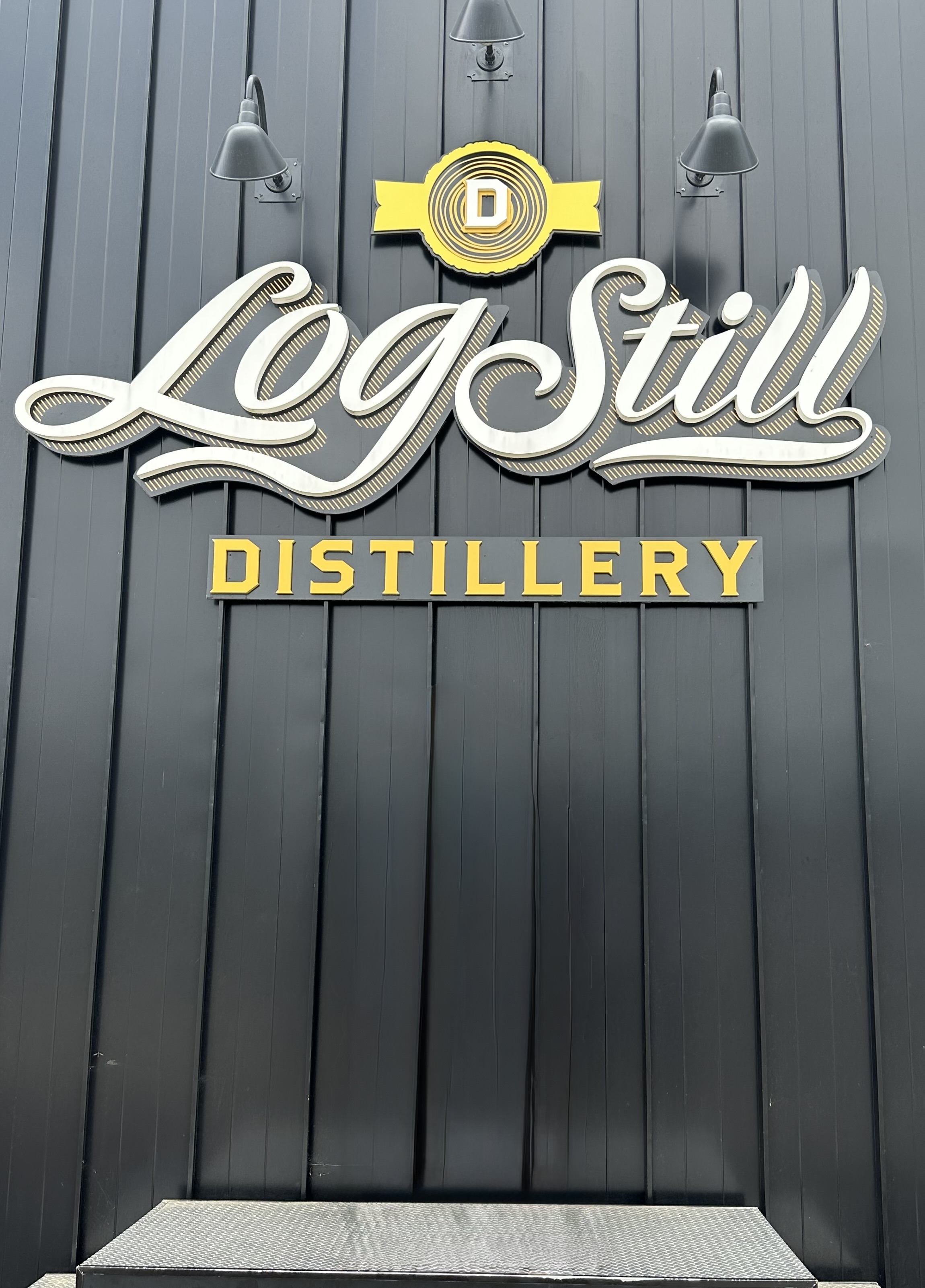 Log Still Distillery logo signage in white and gold script on dark exterior wall