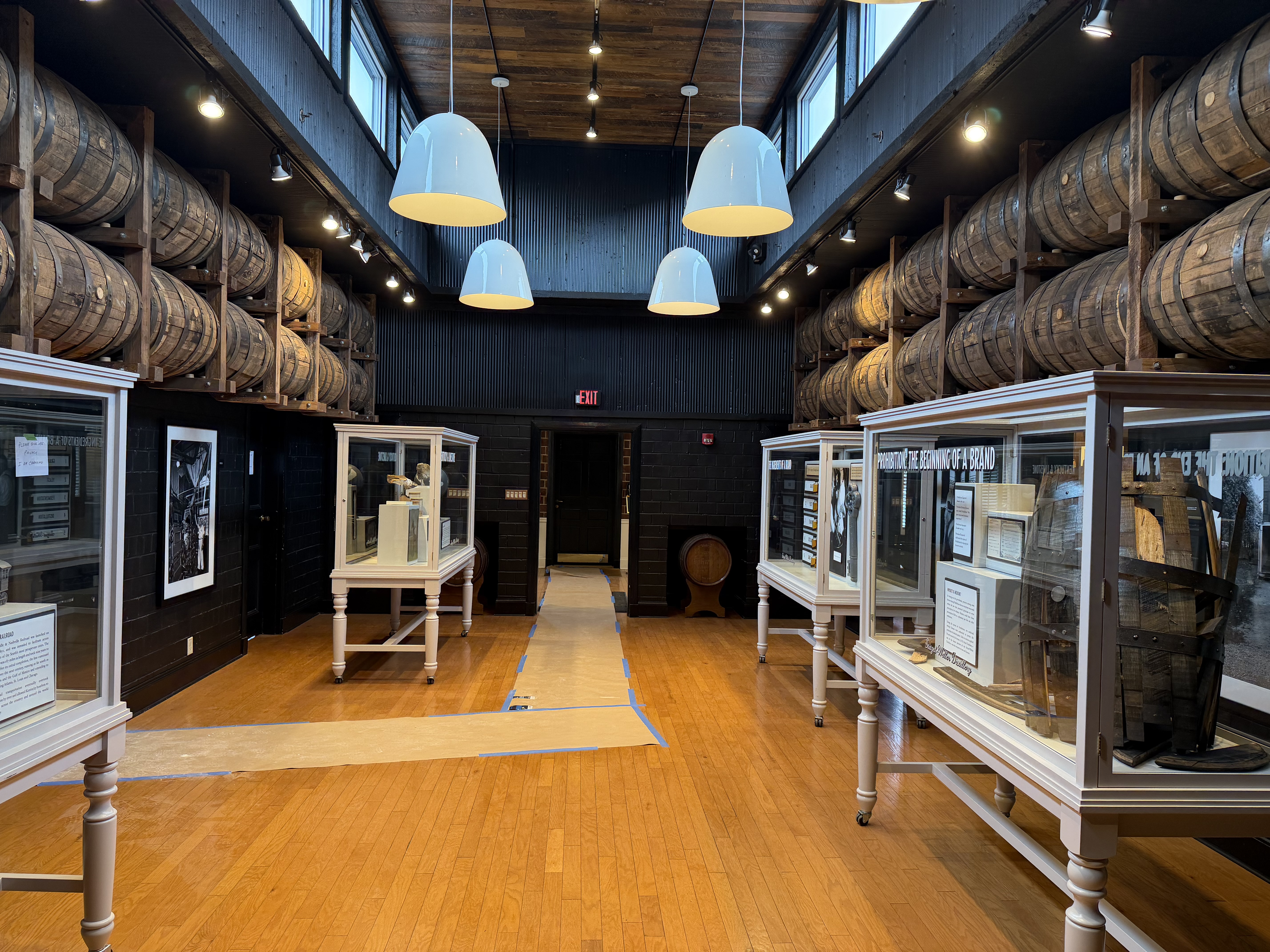 Barrel museum exhibit room inside a Stitzel-Weller rickhouse with aging barrels on racks overhead and historical display cases on the floor